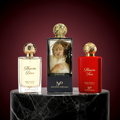 Three perfume bottles from Macdon Perfumes displayed on a black marble pedestal against a dark red background. The center bottle is a 10ml travel size with a black frame and gold cap, featuring a photo of Cee Chronicles on the label.