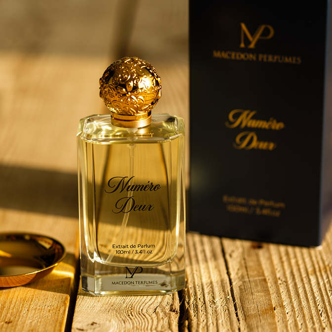 Perfume bottle with gold cap and 'Macedon Perfumes' packaging on a wooden surface